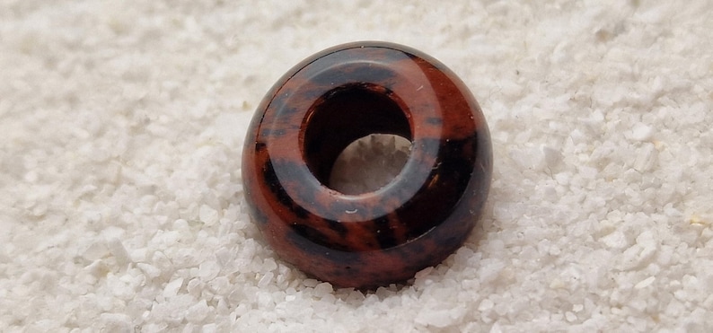 May include: A round, donut-shaped bead made of red and black jasper. The bead has a hole in the center for stringing.