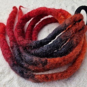 Op de afbeelding: Een set rode, oranje en zwarte ombre wollen dreadlocks met een zwarte haarband.