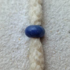 May include: A white braided cord with a blue bead.