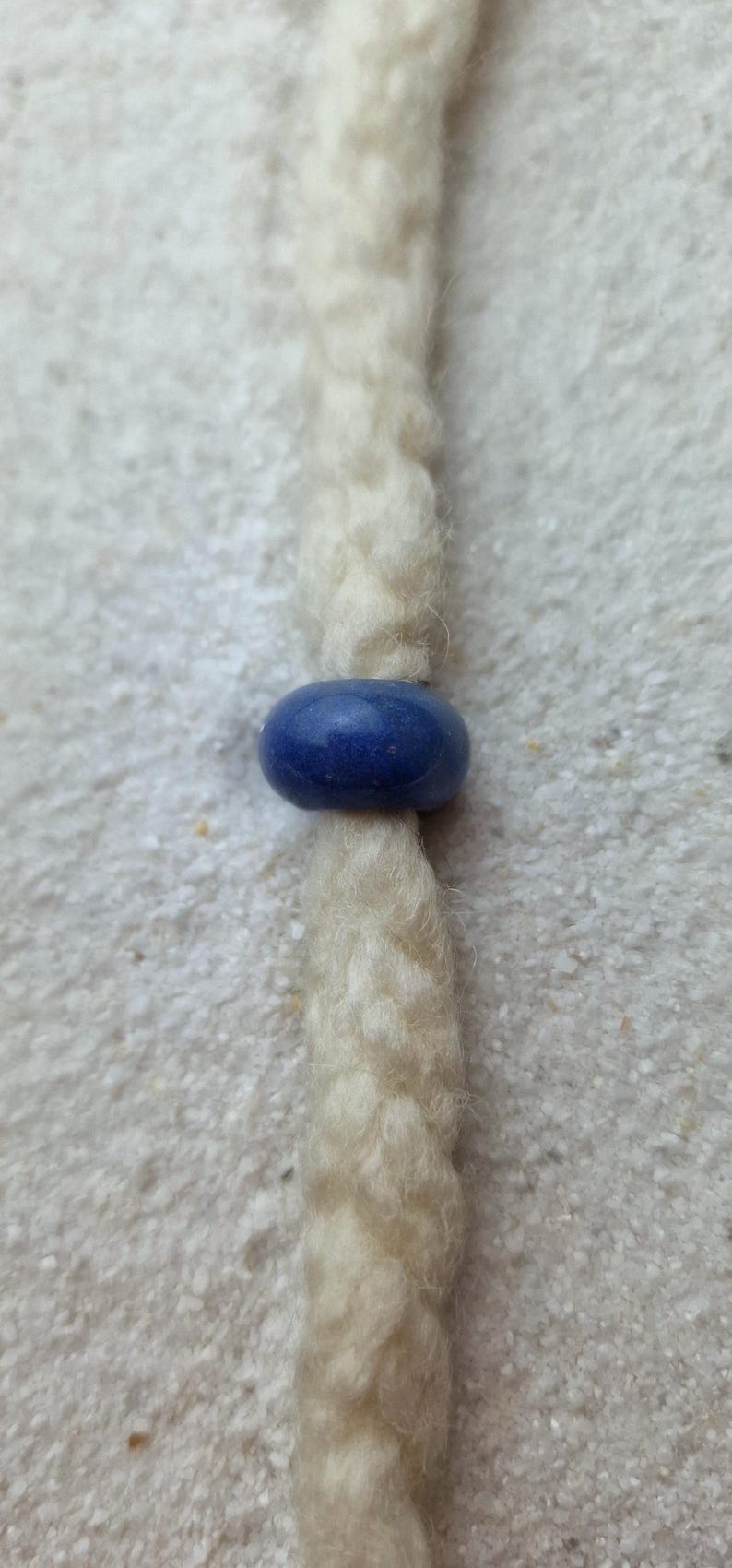May include: A white braided cord with a blue bead.