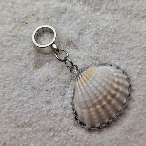 Könnte beinhalten: Ein silberner Anhänger mit einem weißen Muschelanhänger. Der Anhänger ist an einer silbernen Kette befestigt und hat oben einen silbernen Ring.