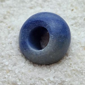 May include: A blue and white ceramic bead with a hole in the center. The bead is round and has a smooth, glossy finish.