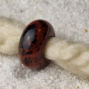 May include: A dark red and black glass bead with a speckled pattern. The bead is round and has a hole in the center for stringing.