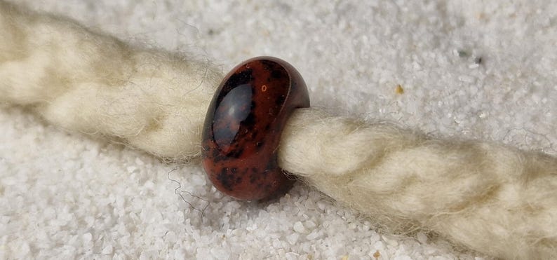 May include: A dark red and black glass bead with a speckled pattern. The bead is round and has a hole in the center for stringing.