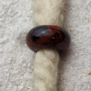 May include: A brown and black glass bead with a shiny finish. The bead is threaded onto a white cord.