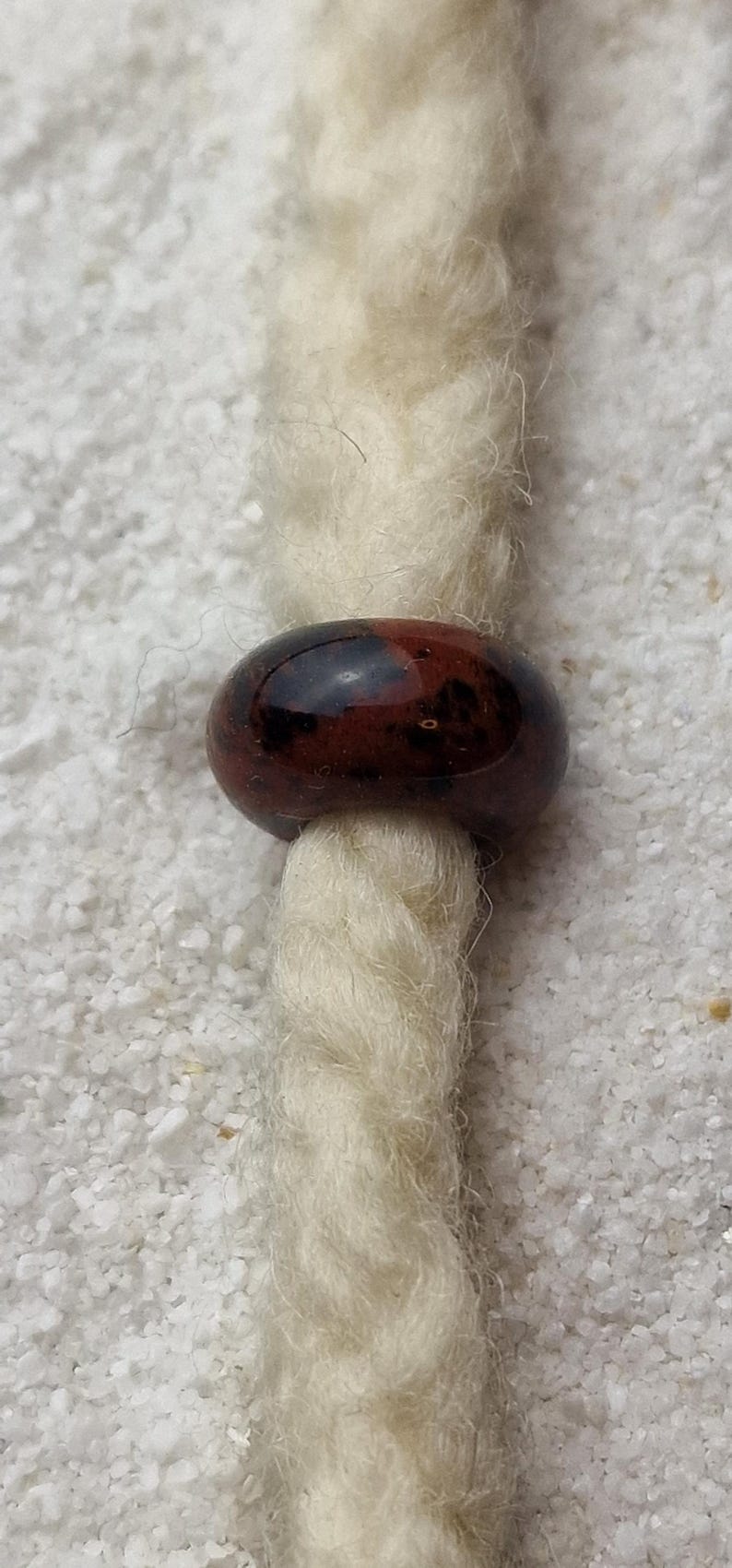 May include: A brown and black glass bead with a shiny finish. The bead is threaded onto a white cord.