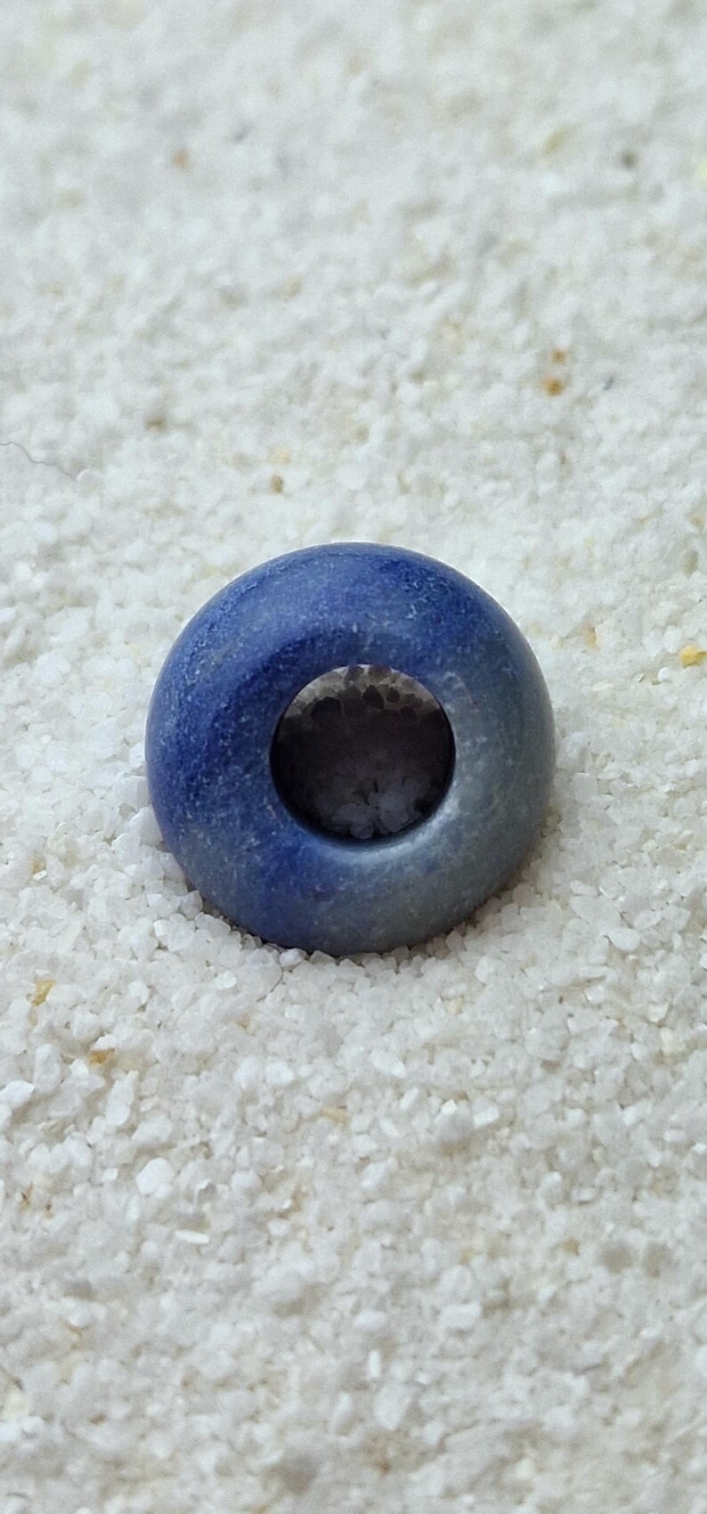 May include: A blue ceramic bead with a hole in the center. The bead has a light blue glaze on one side and a darker blue glaze on the other side.