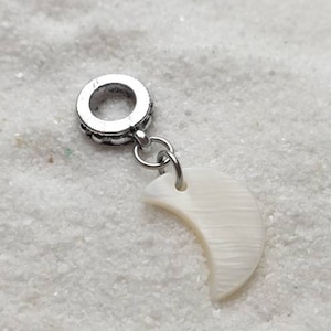 Può includere: Un ciondolo d'argento con un pendente a forma di mezzaluna bianca. Il ciondolo è progettato per essere aggiunto a un braccialetto o una collana.