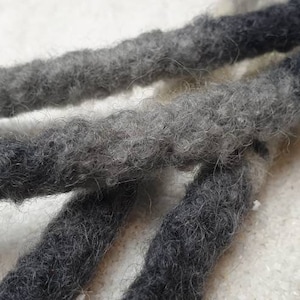 Op de afbeelding: Drie zwarte en grijze ombre dreadlocks gemaakt van wol.