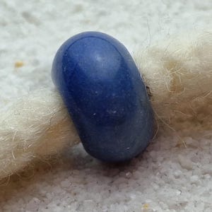 May include: A smooth, round, blue glass bead with a slightly textured surface.