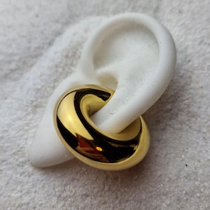 Puede incluir: Un pendiente de doble bucle de color dorado con un acabado liso y brillante.