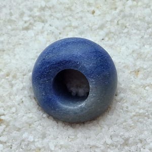 May include: A blue and white ceramic bead with a hole in the center. The bead is round and has a smooth surface.