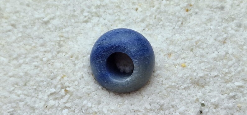 May include: A blue and white ceramic bead with a hole in the center. The bead is round and has a smooth surface.