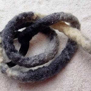 Op de afbeelding: Een dik, handgesponnen garen van wol in grijstinten en wit. Het garen is gedraaid in een touwachtige vorm en is opgerold in een cirkel.