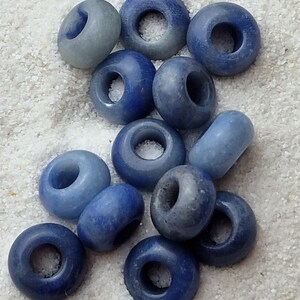 May include: A collection of blue and light blue donut-shaped beads with a hole in the center. The beads are arranged in a pile on a white surface.