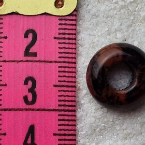 May include: A brown and black ring-shaped bead with a hole in the center. The bead is about 1 inch in diameter.