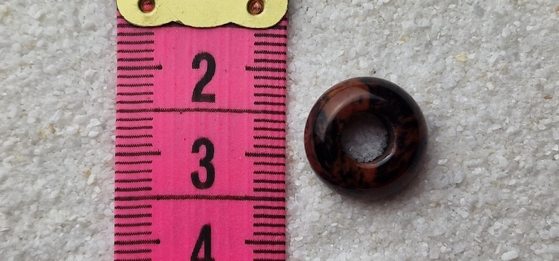 May include: A brown and black ring-shaped bead with a hole in the center. The bead is about 1 inch in diameter.