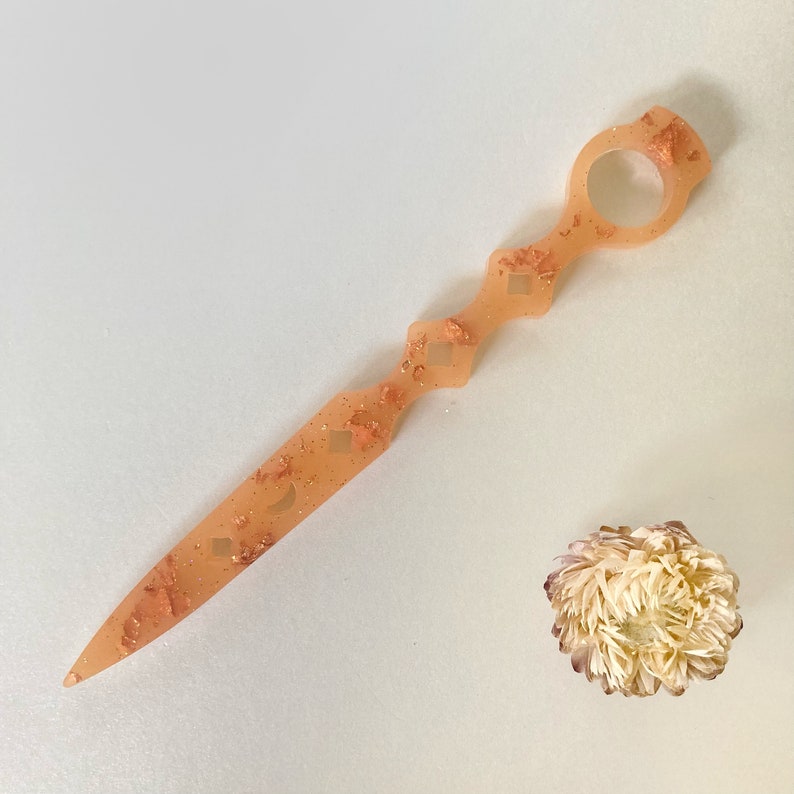 Op de afbeelding: Een perzikkleurige plastic haarspeld met een decoratief ontwerp met gouden glitter en een rond handvat.