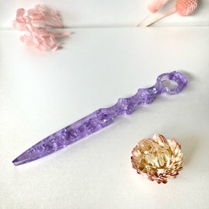 Op de afbeelding: Een paars, doorschijnend, decoratief mes met zilveren glitter ingebed in het plastic. Het mes heeft een unieke, gebogen handgreep met een gat in het midden.