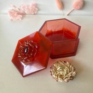 May include: A red hexagonal trinket box with a floral design on the lid. The box is open and the inside is visible.