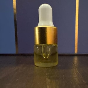 May include: A small glass dropper bottle with a gold-colored band and a white dropper top. The bottle contains a clear, yellowish liquid. The background is a dark blue with gold vertical stripes.