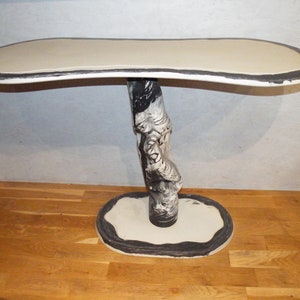Peut inclure: Une console unique faite à la main avec un plateau ovale de couleur crème. Le bord de la table est souligné en noir. La base est un design artistique sculpté en noir et blanc, soutenu par une base ovale. La table mesure environ 122 cm de long.