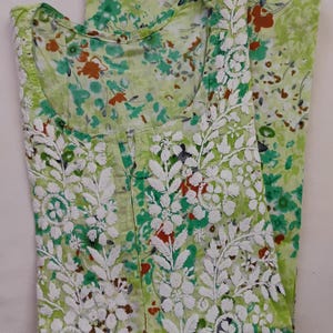 May include: A light green floral print garment with white embroidered floral and leaf patterns. The garment has a round neckline and is folded, showing the front and part of the back. The floral print includes red, green, and white accents.