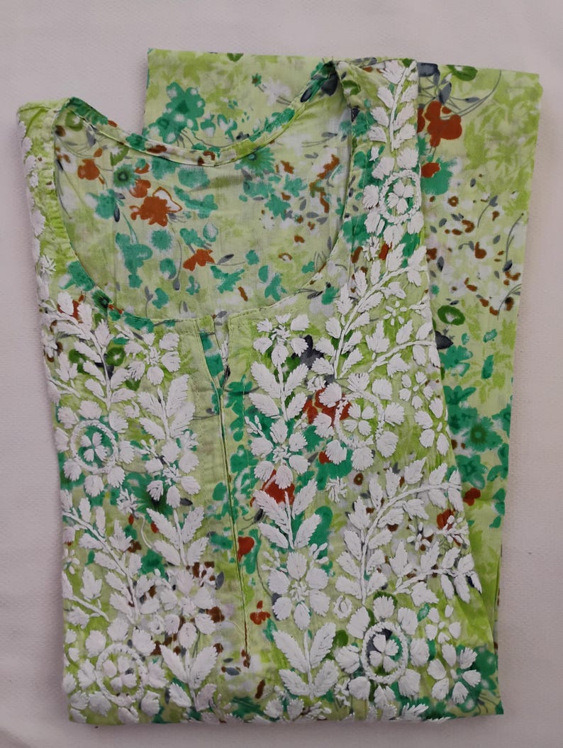 May include: A light green floral print garment with white embroidered floral and leaf patterns. The garment has a round neckline and is folded, showing the front and part of the back. The floral print includes red, green, and white accents.