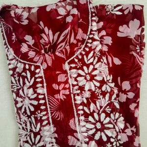 以下が含まれることがあります： 白の花柄が施されたマルーン色の衣服。丸いネックラインがあり、白いステッチで装飾されています。花柄は生地全体に見られます。