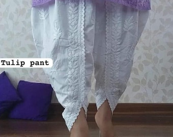 Può includere: Pantaloni bianchi a forma di tulipano con bordino in pizzo bianco e ricamo. I pantaloni hanno una forma a tulipano e sono realizzati in un tessuto leggero.