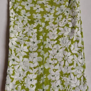 May include: A lime green tunic with white floral embroidery. The tunic has a V-neck and a detailed floral pattern. The embroidery creates a textured design, suitable for casual wear. The tunic is made of a lightweight fabric.
