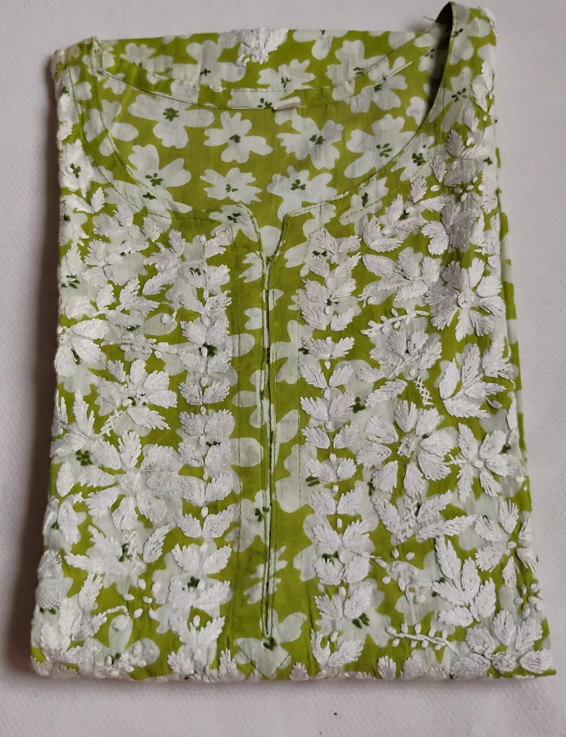 May include: A lime green tunic with white floral embroidery. The tunic has a V-neck and a detailed floral pattern. The embroidery creates a textured design, suitable for casual wear. The tunic is made of a lightweight fabric.