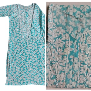 May include: A turquoise tunic with white floral embroidery. The long-sleeved tunic features a round neckline and a buttoned placket. The fabric is patterned with small white flowers and detailed embroidery around the neckline and cuffs.