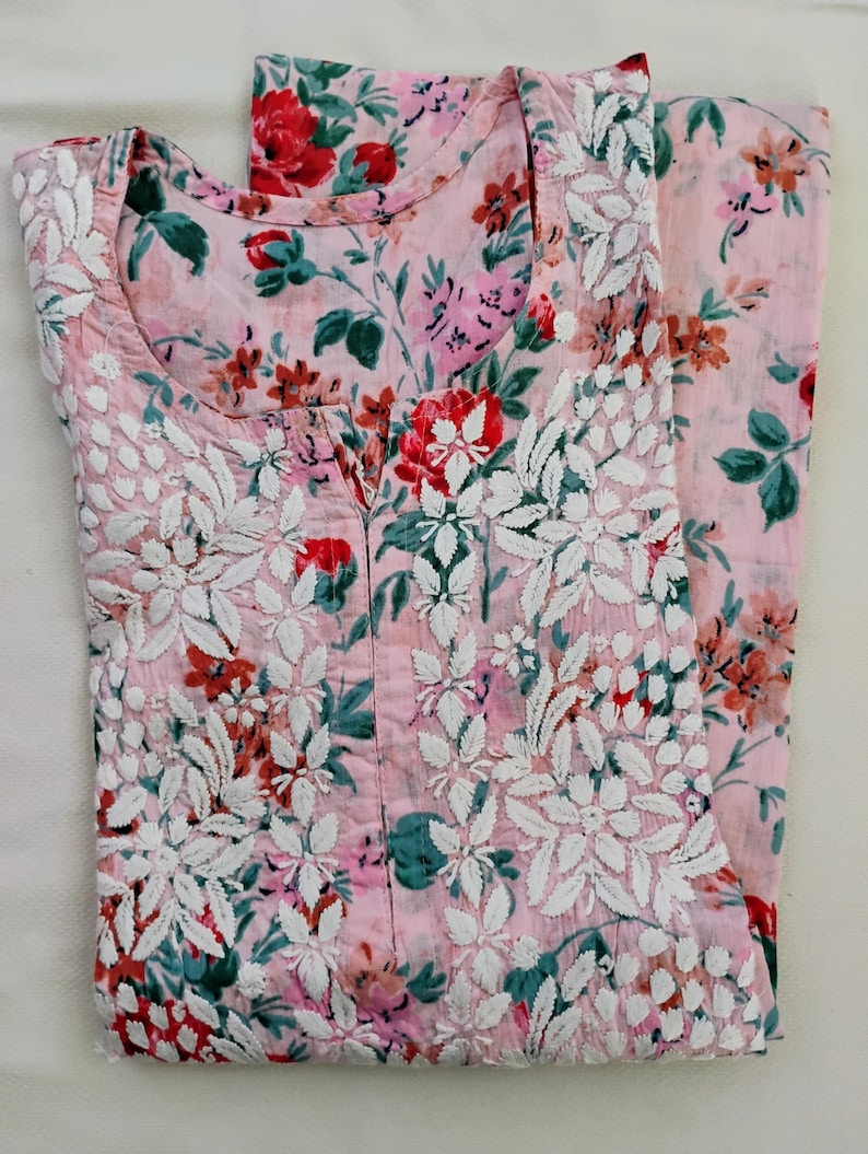 May include: A light pink floral print outfit, comprising a top and trousers. The top features a scoop neckline and white floral embroidery. The floral pattern incorporates red, pink, and green hues, offering a vibrant and feminine aesthetic.