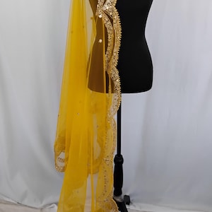 May include: A bright yellow sheer dupatta, a traditional Indian scarf, draped on a black mannequin. The dupatta features intricate gold embroidery along the edges, with delicate beadwork and sequin embellishments. The fabric is lightweight and flowing.