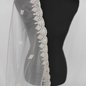 May include: A sheer white dupatta or shawl featuring a scalloped edge with intricate embroidery in silver and pale pink thread. The fabric is adorned with small, repeating diamond-shaped motifs scattered across the translucent material.