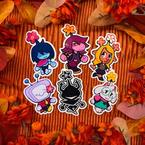 May include: A set of six die-cut stickers featuring cartoon characters including a blue-haired figure, a purple-haired character, a yellow deer-like creature, a television-headed figure, a black silhouette, and a white goat-like character.