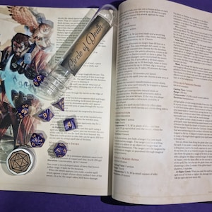 May include: A close-up of a book open to a page with the title "Circle of Death" and a description of the spell "Crushing Prison".  The book is surrounded by several purple and blue dice, a clear tube with a label that says "Circle of Death", and a small metal container with a brown lid.