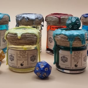 May include: Six small glass jars with colourful wax seals and labels that say "D20 Potion Dice Roller" and "Brewed by [unclear text]"  The jars are arranged in a semi-circle on a white surface. There are also two 20-sided dice, one blue and one brown, on the surface.