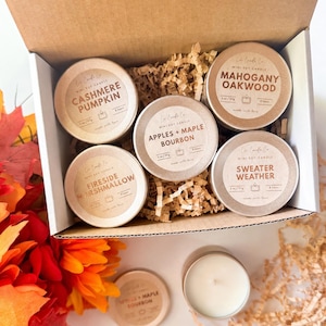Peut inclure: Une boîte cadeau en carton contenant cinq boîtes rondes en métal de bougies au soja avec des étiquettes indiquant Cashmere Pumpkin, Mahogany Oakwood, Apples + Maple Bourbon, Fireside Marshmallow et Sweater Weather, pesant 2 oz/57g chacune.
