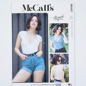 May include: McCall's sewing pattern M8407 featuring a top design. The pattern includes images of the top in white and light blue. The pattern is designed and printed in the USA. The size range is Y5 (18-20-22-24-26).