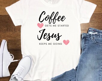 May include: White t-shirt with the text "Coffee gets me started, Jesus keeps me going" in black script. Two pink hearts accent the text. The shirt is paired with blue jeans and white sneakers.