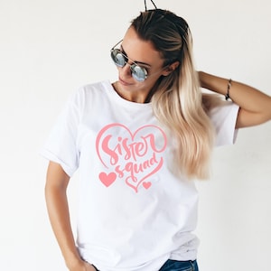 May include: White t-shirt with a pink heart design and the text "Sister Squad" inside the heart.