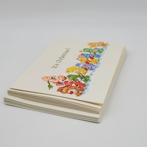 May include: A stack of Christmas cards with a festive illustration. The cards feature a colourful design of teddy bears, candy canes, and the text "It's Christmas!" in a whimsical font. The cards are on a white background.
