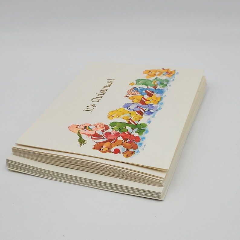 May include: A stack of Christmas cards with a festive illustration. The cards feature a colourful design of teddy bears, candy canes, and the text "It's Christmas!" in a whimsical font. The cards are on a white background.