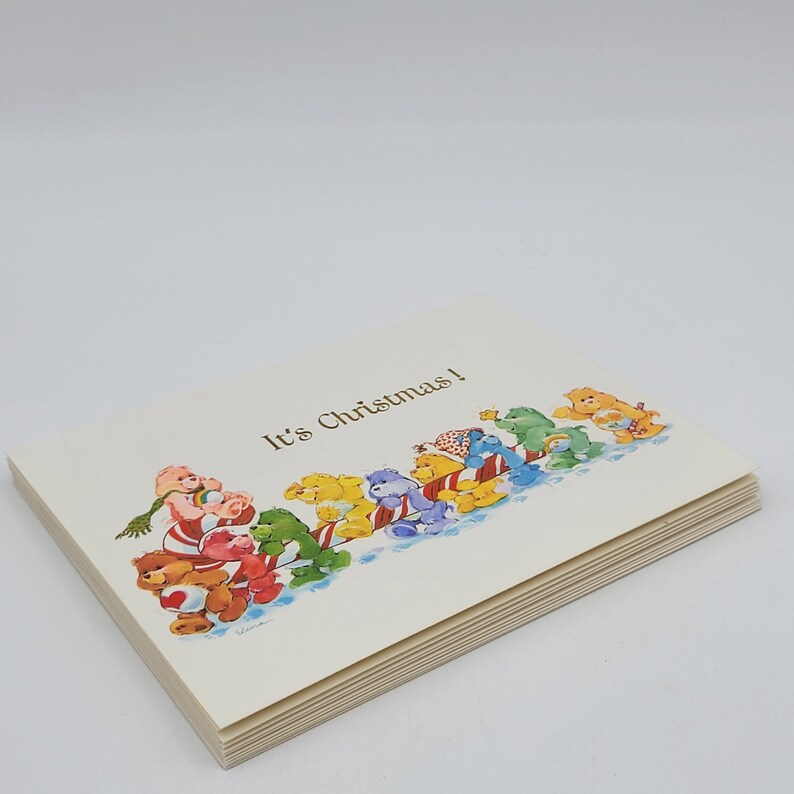 May include: A stack of greeting cards with a cream background. The cards feature a colourful illustration of cartoon bears pulling a sled, with the text "It's Christmas!" printed on the front.