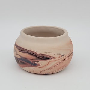 May include: A small, round, ceramic pot with a marbled design in shades of brown, orange, and white.