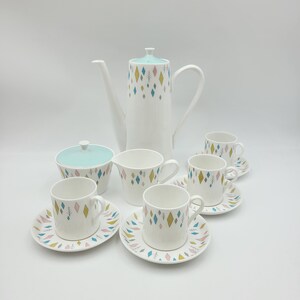 May include: A vintage tea set featuring a geometric pattern in shades of blue, green, and yellow. The set includes a teapot, sugar bowl, creamer, and four cups and saucers.
