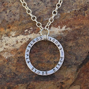 Puede incluir: Collar de plata con un colgante redondo que dice "Stude et Disce, Iudice Conte" en un patrón circular.