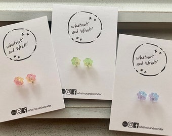 May include: Three cards with paw print earrings on them. The cards are white with black text that says "whatnot and Wonder" and social media icons. The earrings are in pink, green, and blue.